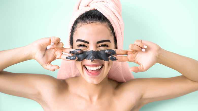 young woman  putting on a clay mask and smiling