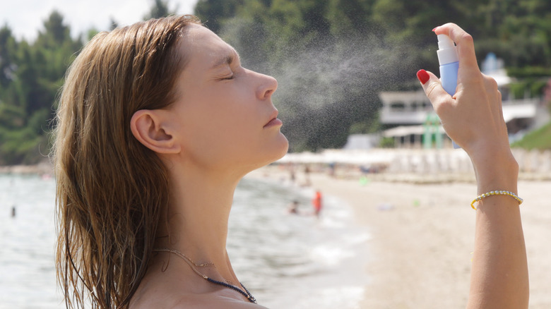 woman sprays her face with sunscreen