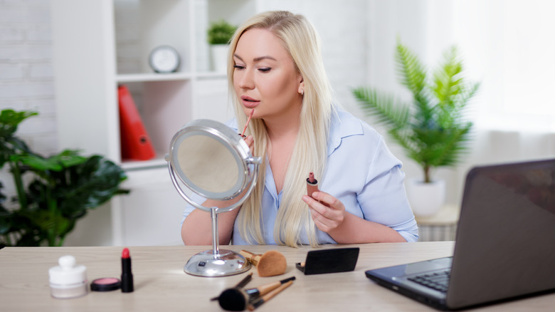 Woman putting on lipgloss at desk