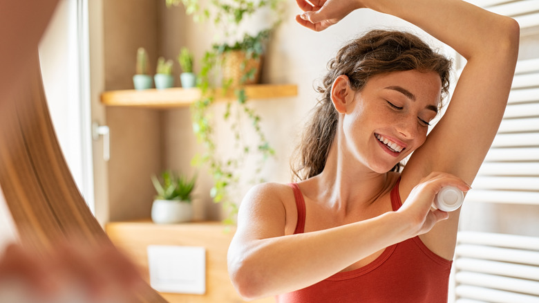 Girl applying antiperspirant to underarms in bathroom mirror