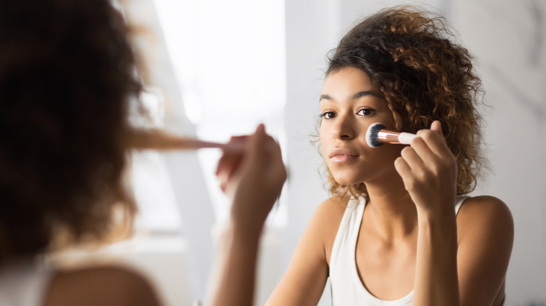 Woman applying makeup in mirror