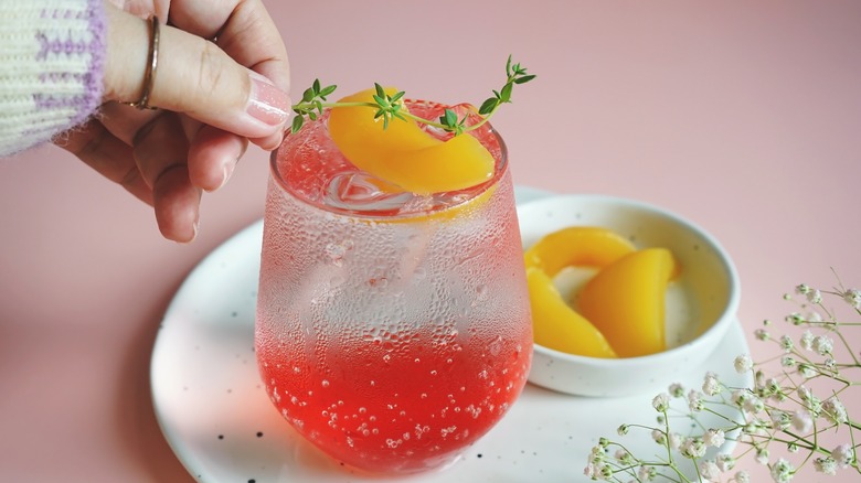 Person placing thyme on fruit flavored sparkling water