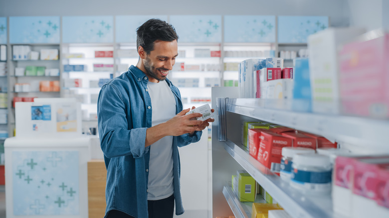 man in pharmacy store aisles looking at medicine