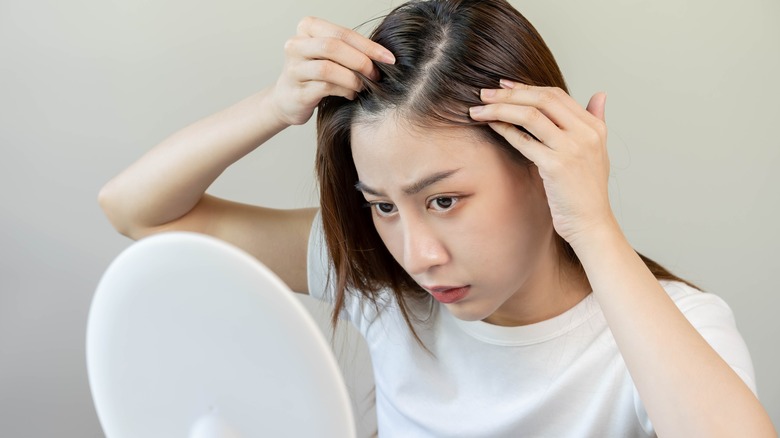 Asian woman examining scalp in mirror