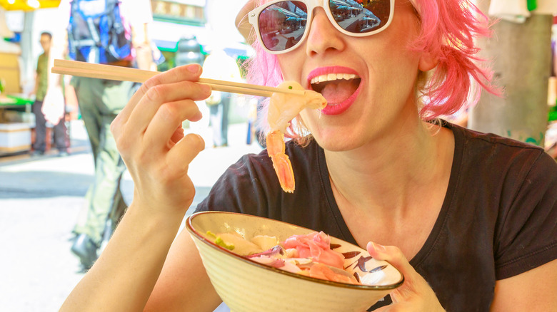 women with pink hair eating fish with chopsticks