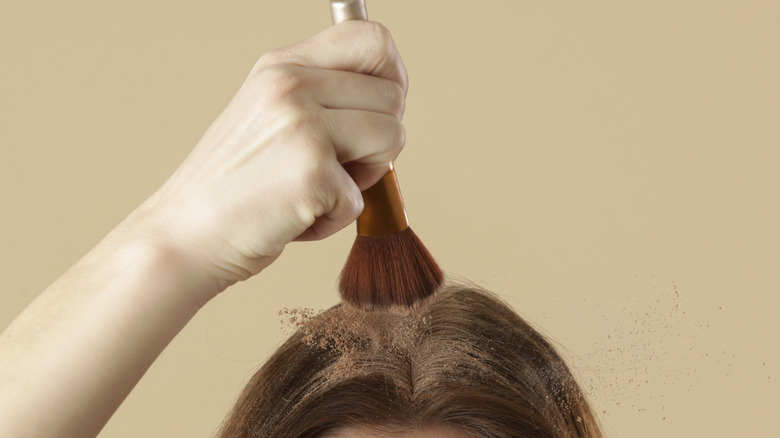 Person dusting cocoa powder dry shampoo onto scalp