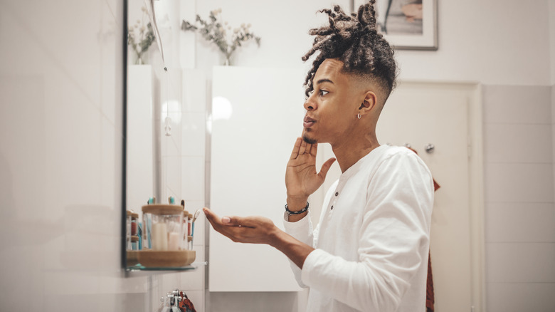 Young man applying skincare to face