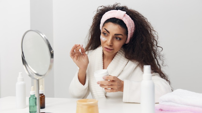 woman applying facial cream on cheek 