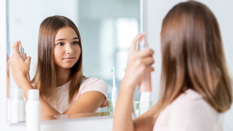 woman looking into mirror sprays hair mist onto her hair