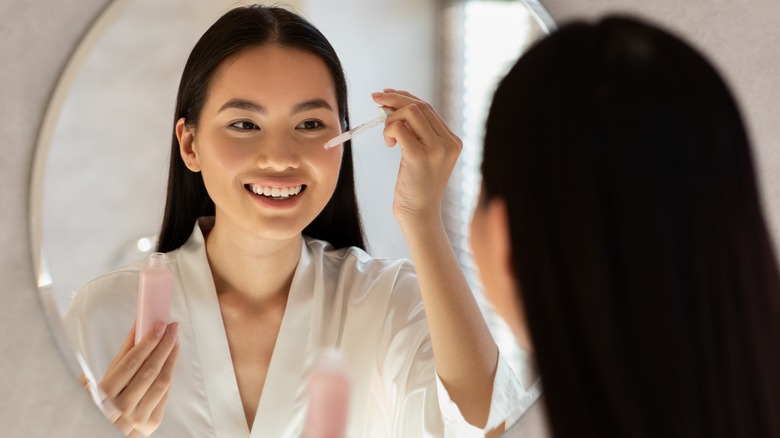 Model putting on face serum in the mirror