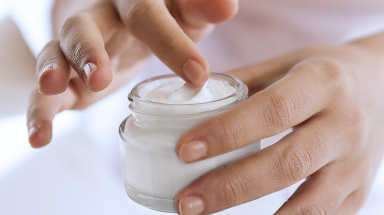 Finger touching jar of cream