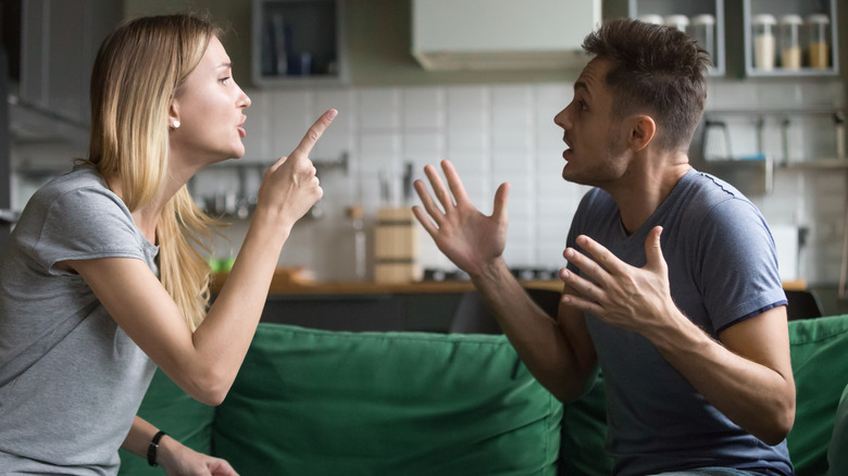 man and woman sitting on the couch, woman yelling at man, man throwing up his hands