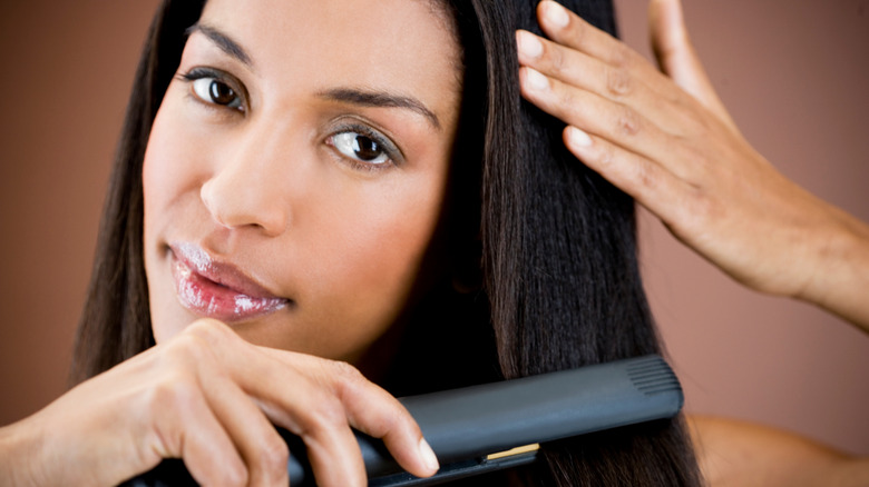 Black woman straightening hair with flat-iron