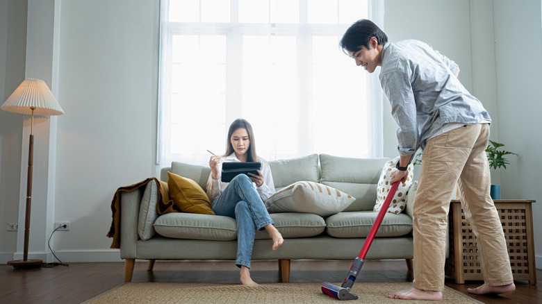 man vacuums while woman works