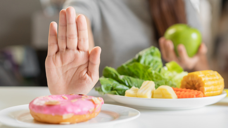 young woman holding fruit and veggies and pushing away donut