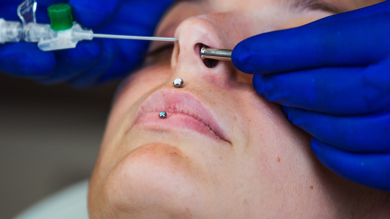 Woman receiving nose piercing treatment