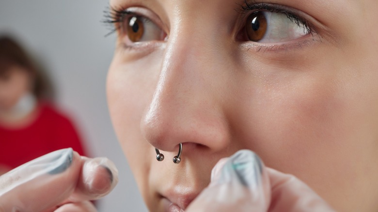 Close up of person's septum piercing being assessed by piercer