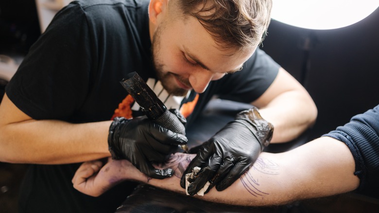 Male tattoo artist inking arm tattoo
