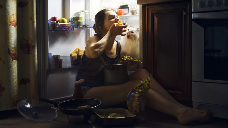 Woman eating next to refrigerator with cat