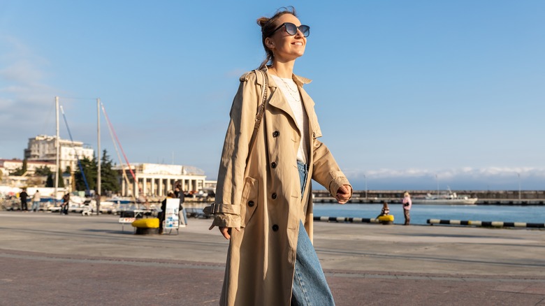 woman walking with a trench coat, white tee and blue jeans