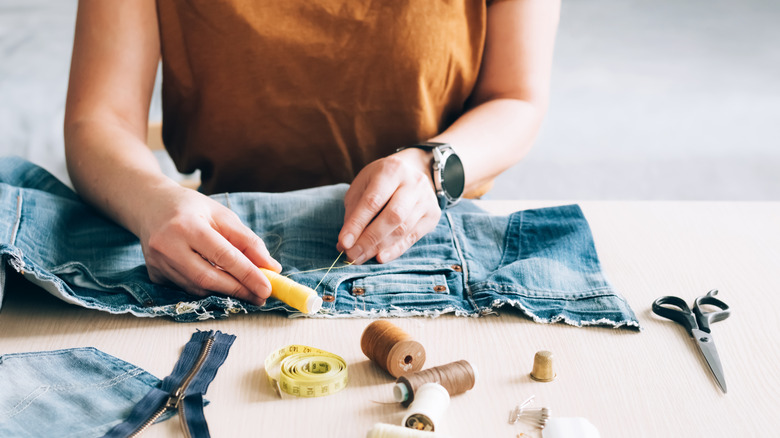 woman repurposing jeans with thread and scissors 