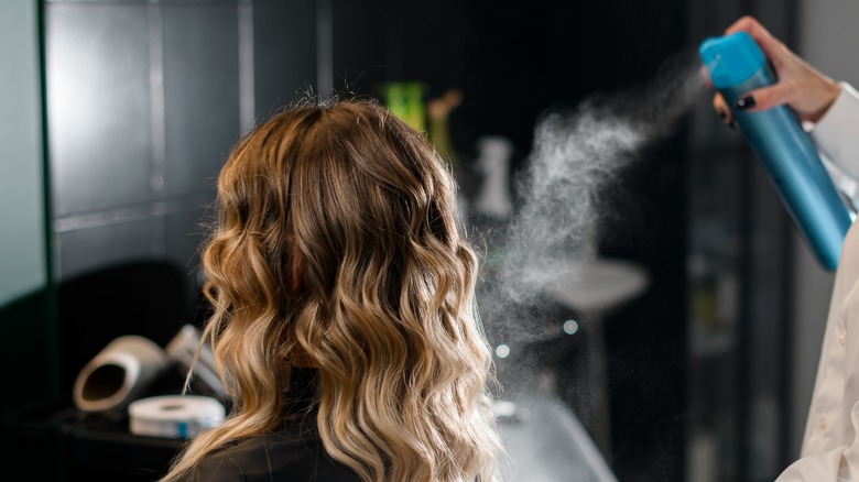 Person spraying hairspray onto curls