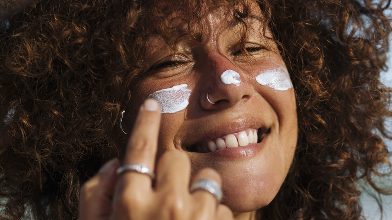 Smiling woman applying sunscreen to face