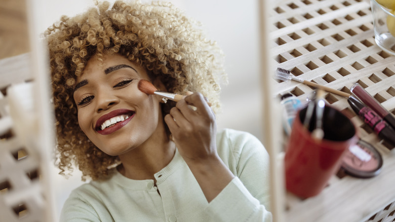 smiling woman applying powder blush 