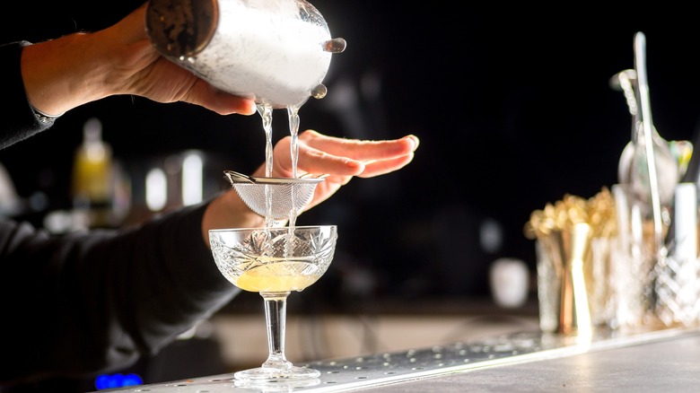 Bartender strains a cocktail into a glass