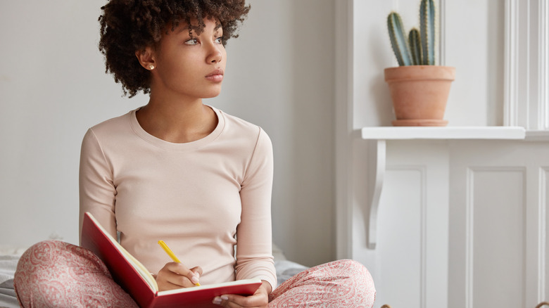 Woman looks out window while journaling