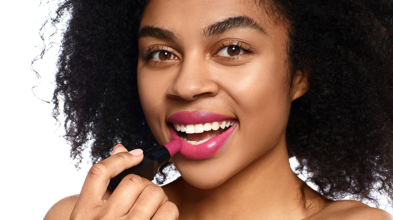 Woman putting on magenta lipstick