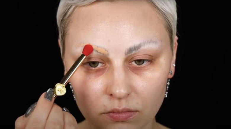 A makeup artist covering her brow with concealer against a black background