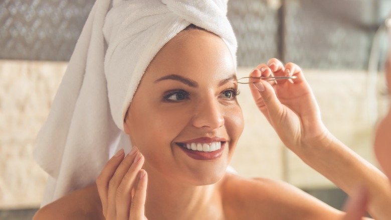 A woman tweezing her eyebrows to hop on the skinny brow trend