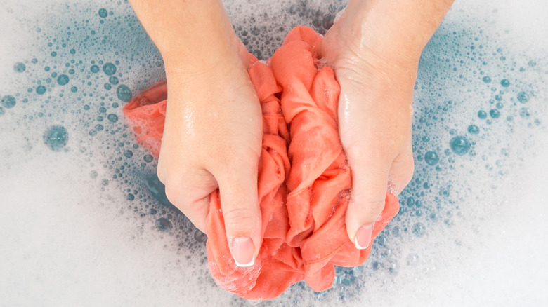 Hands with manicured nails washing red fabric