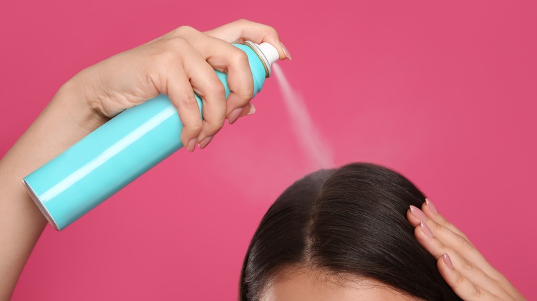 Woman spraying dry shampoo on scalp 