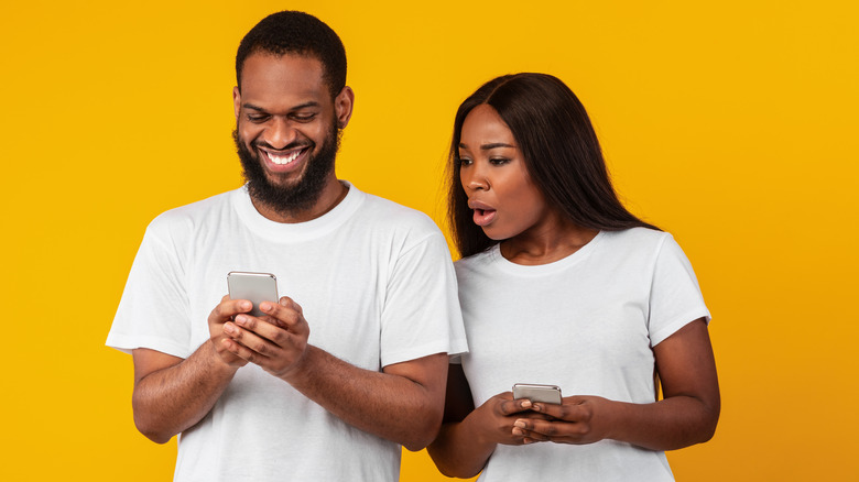 A shocked partner checking her smiling partner's phone