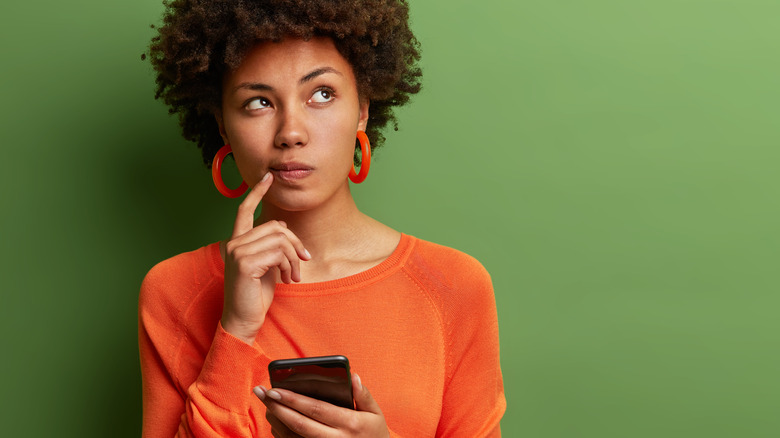 woman holding phone thinking