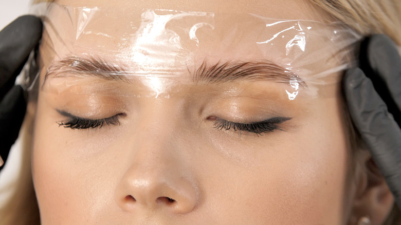 woman applying saran wrap on brows 