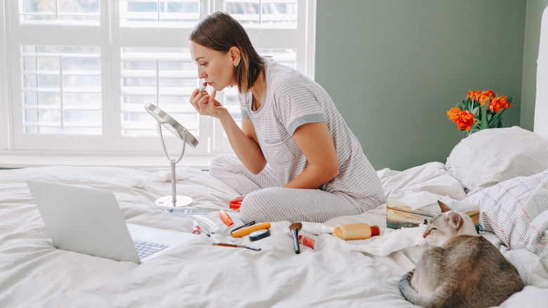 Woman applying makeup on bed