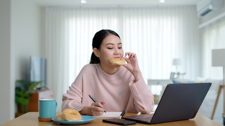 woman at desk eating doughnut