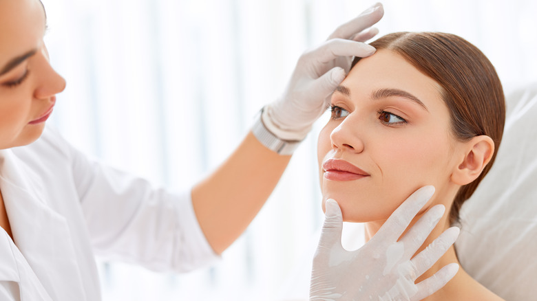 doctor with white gloves examining woman's face in office