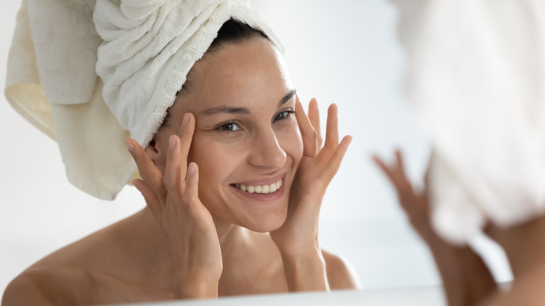 woman examining face in mirror with towel around hair
