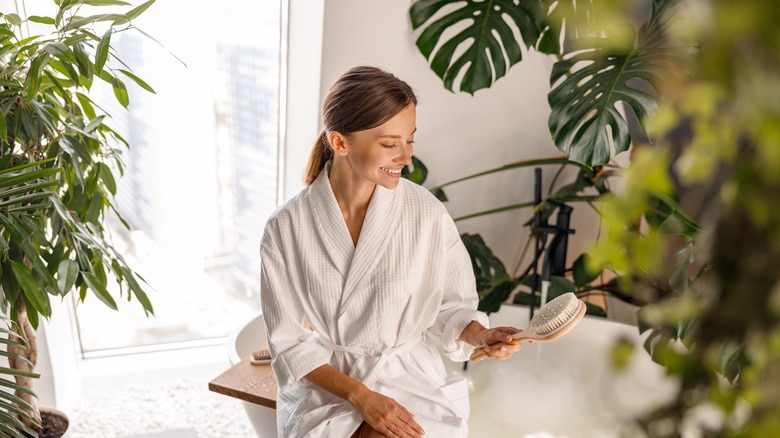 woman in bathrobe looking at a brush with plants