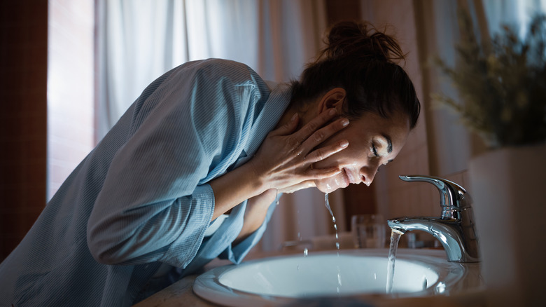 woman washing face at night in pajamas at the sink