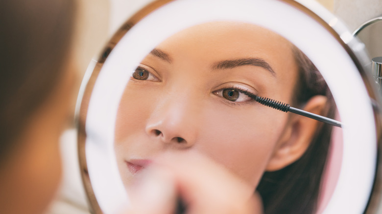 Woman applying mascara in lighted mirror
