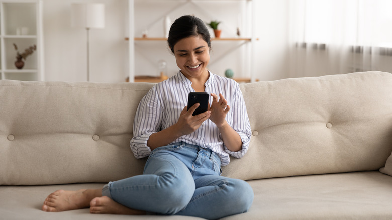 woman texting and smiling on couch