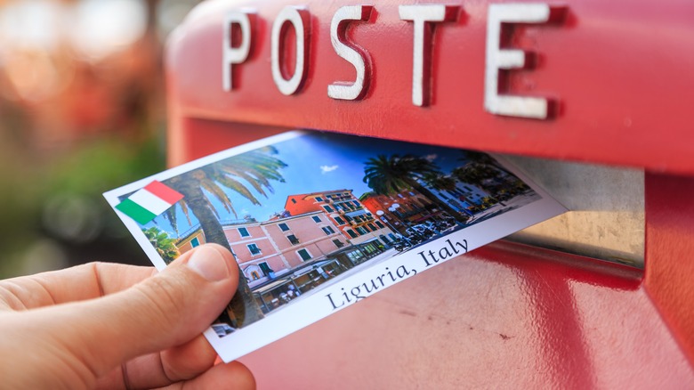 Someone putting a postcard into a mailbox