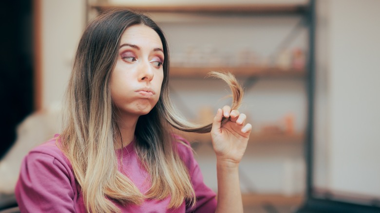 woman pulling at broken hair in mirror