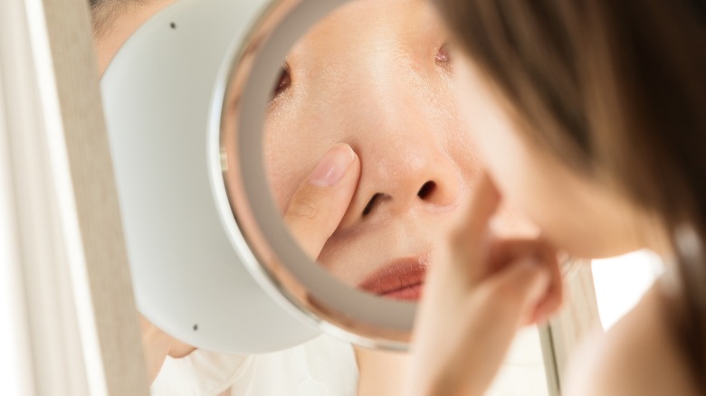 woman looking at nose in mirror