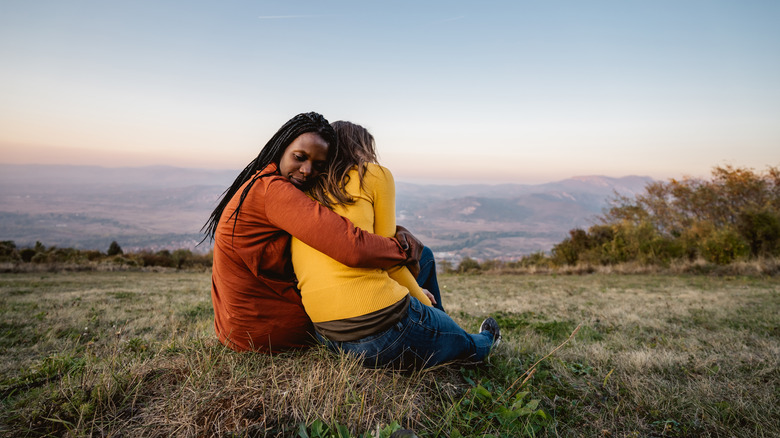 two friends sitting in field hugging